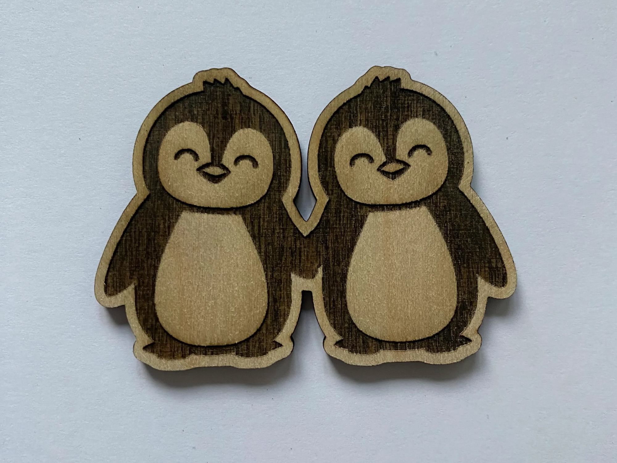 Two cute wooden penguins holding hands as a paired ornament
