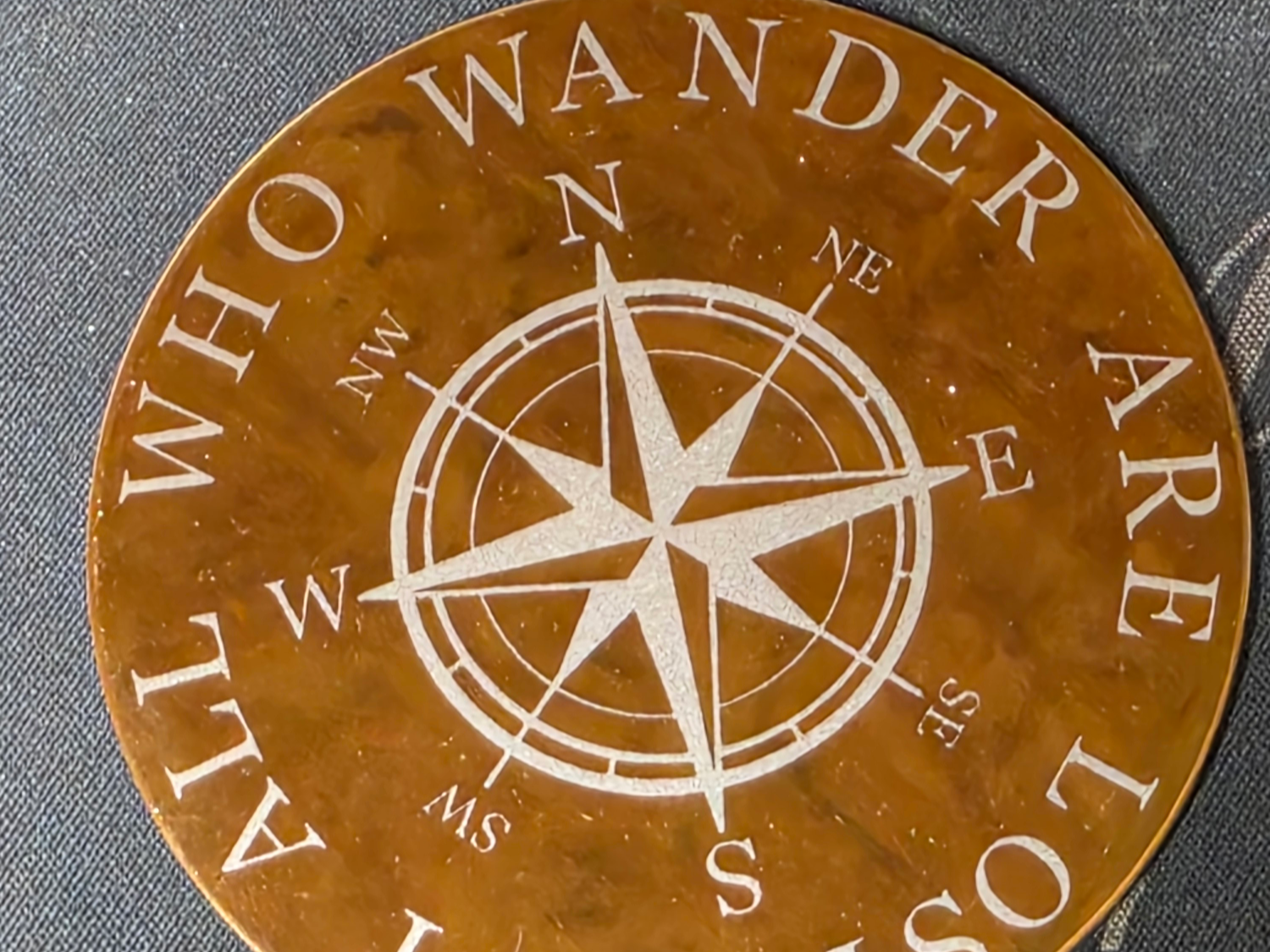 Metal coaster engraved with a compass and travel-inspired quote