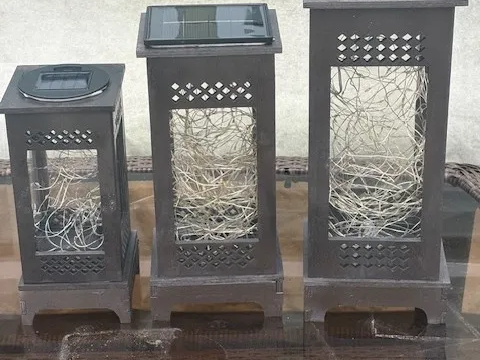 Three dark framed solar lanterns filled with fairy lights on a deck outdoor light idea