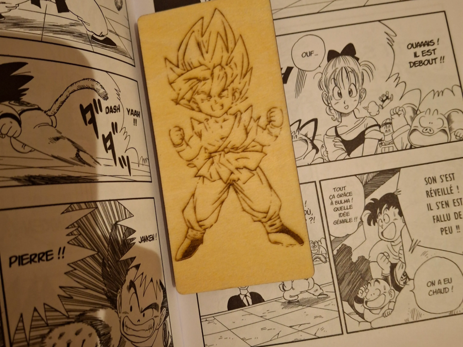 超サイヤ人悟空が刻まれた木製しおり、ドラゴンボールのマンガ巻の中に置かれている