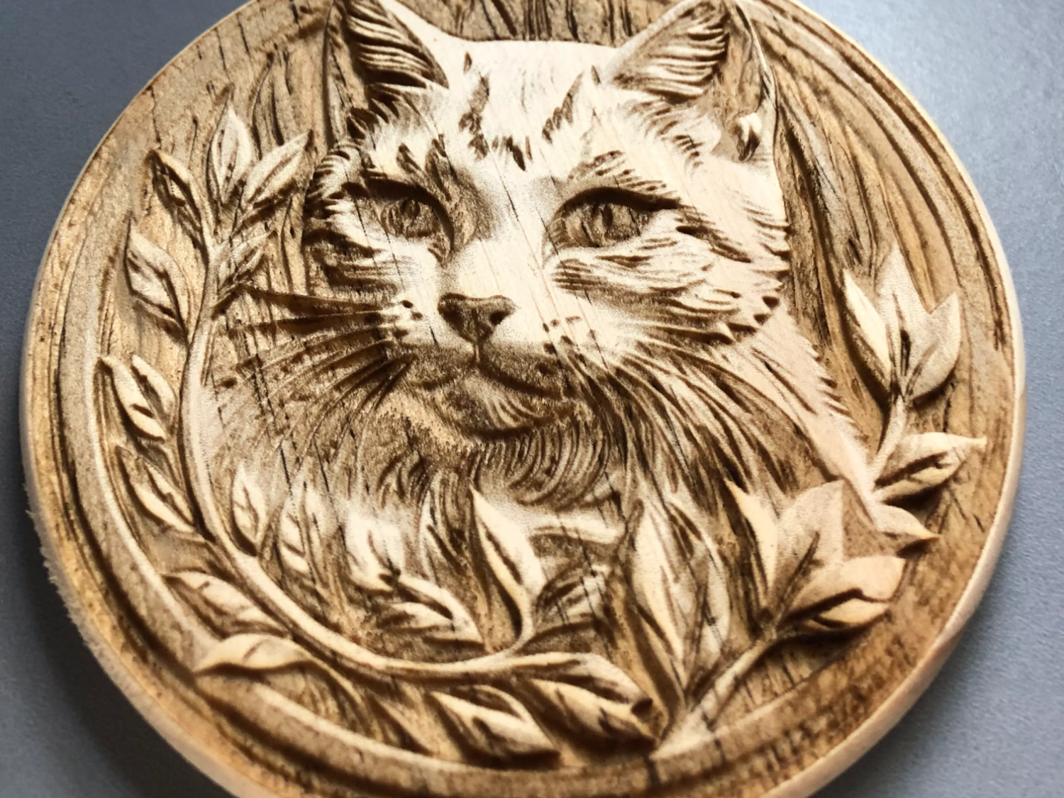 Round wood coaster with a carved relief cat photo portrait inside a leaf border