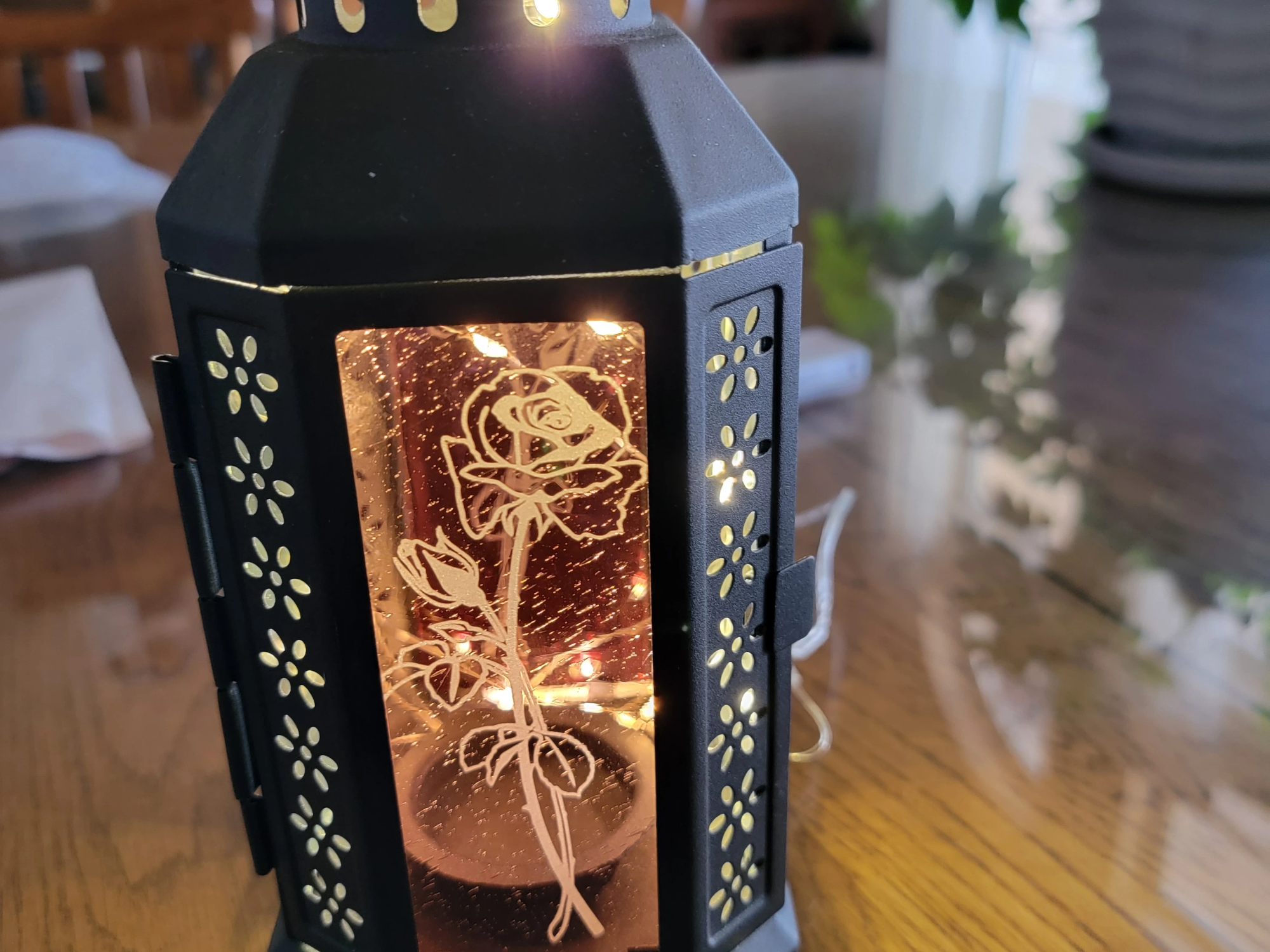 Black metal lantern with etched rose floral motif on a copper toned panel outdoor lantern idea