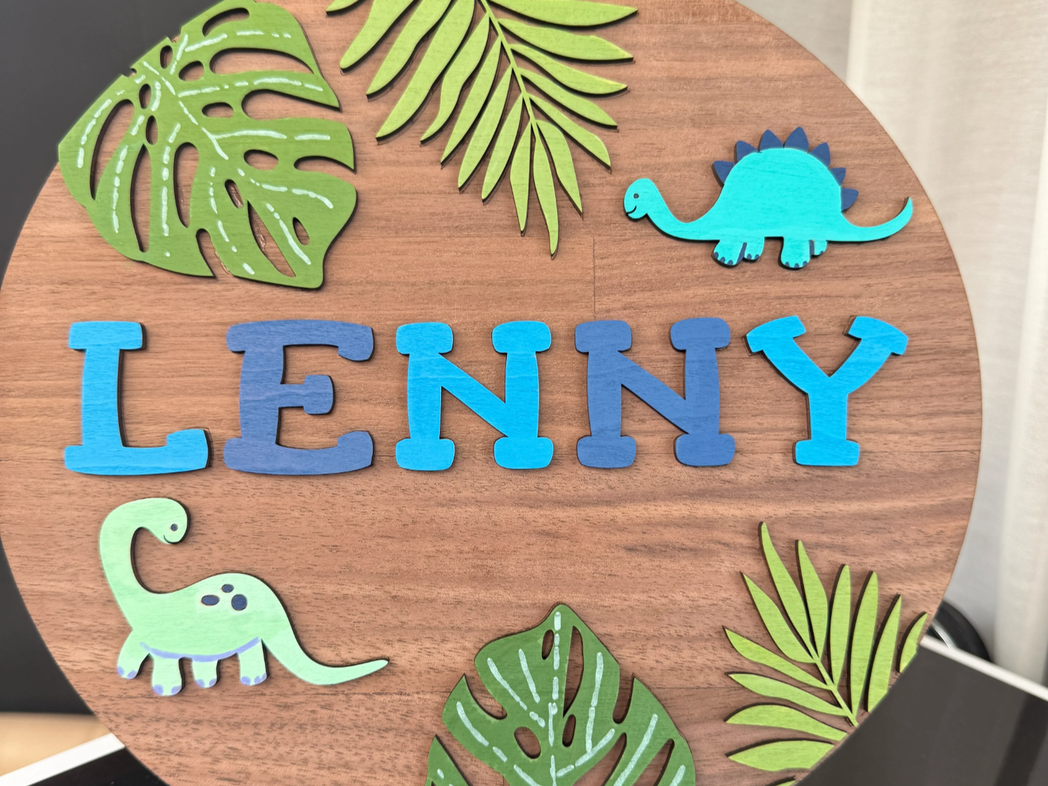 Wooden name sign decorated with cut dinosaur and leaf shapes