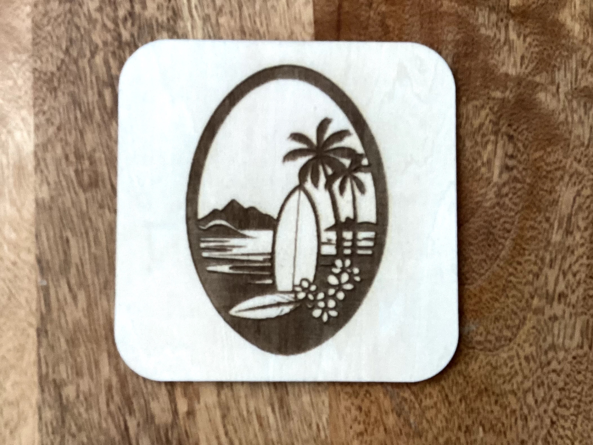 Wooden square coaster engraved with a beach and surfboard scene