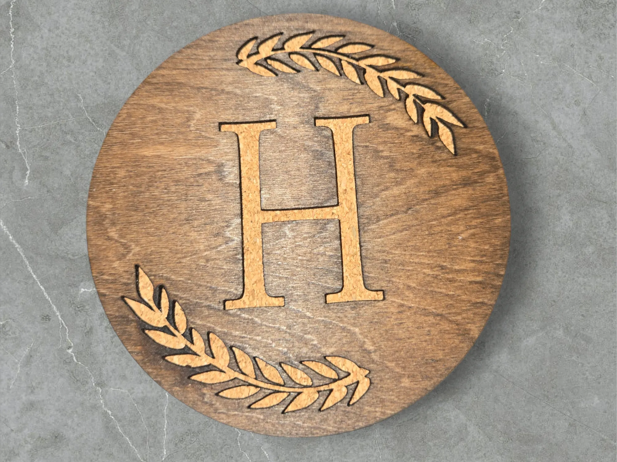 A wood coaster with a monogram framed by a laurel wreath