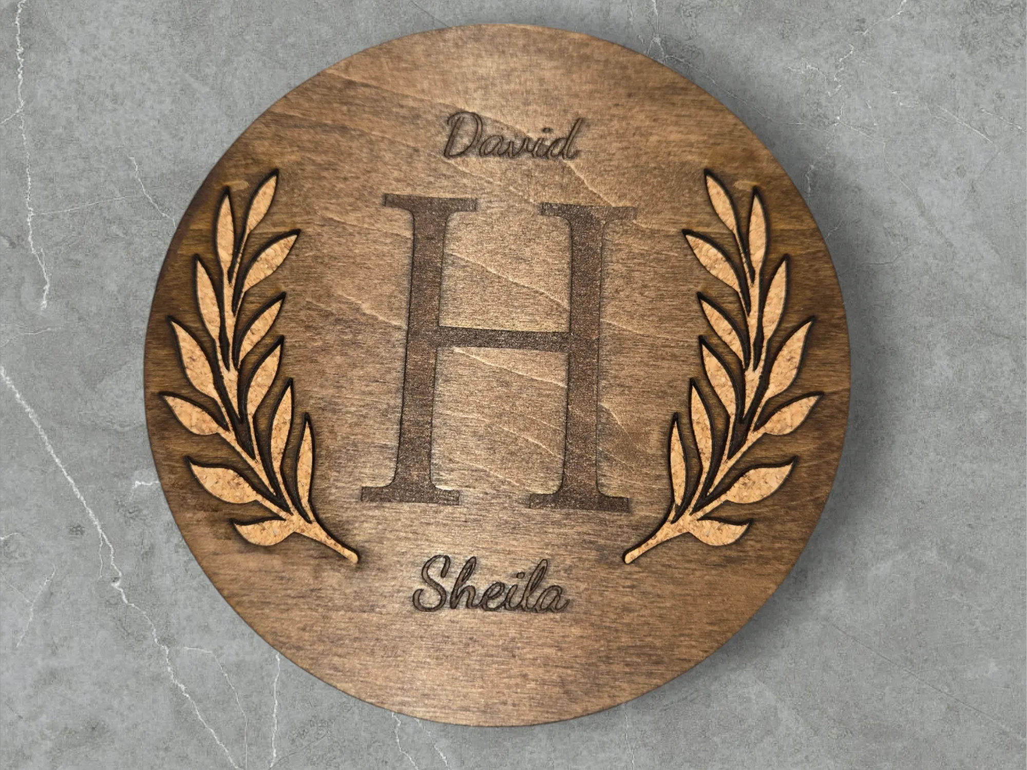 Monogramme familial encadré d'une couronne de laurier, gravé sur un dessous de verre rond en bois