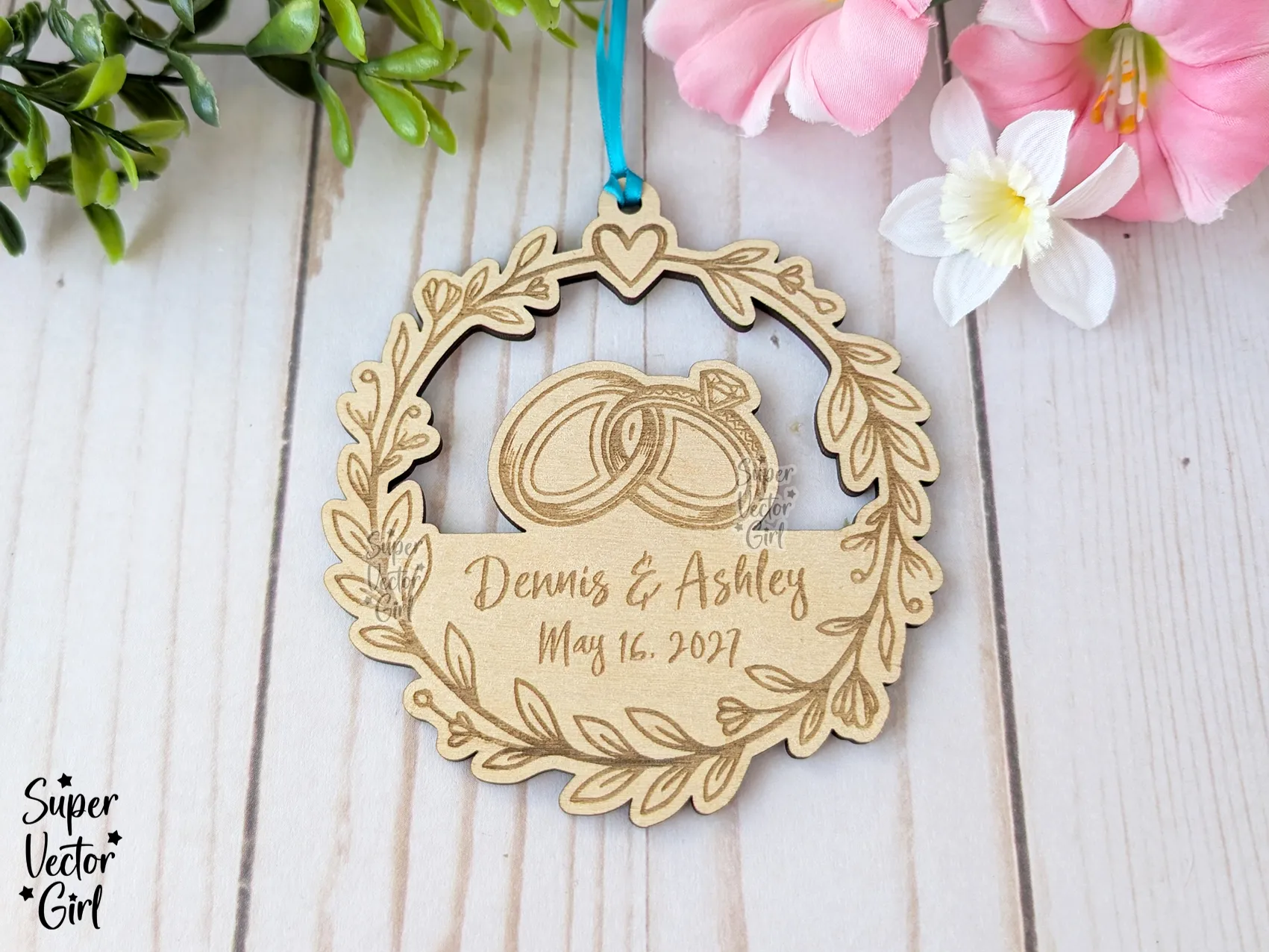 A wooden wreath ornament with engraved rings, names, and a wedding date