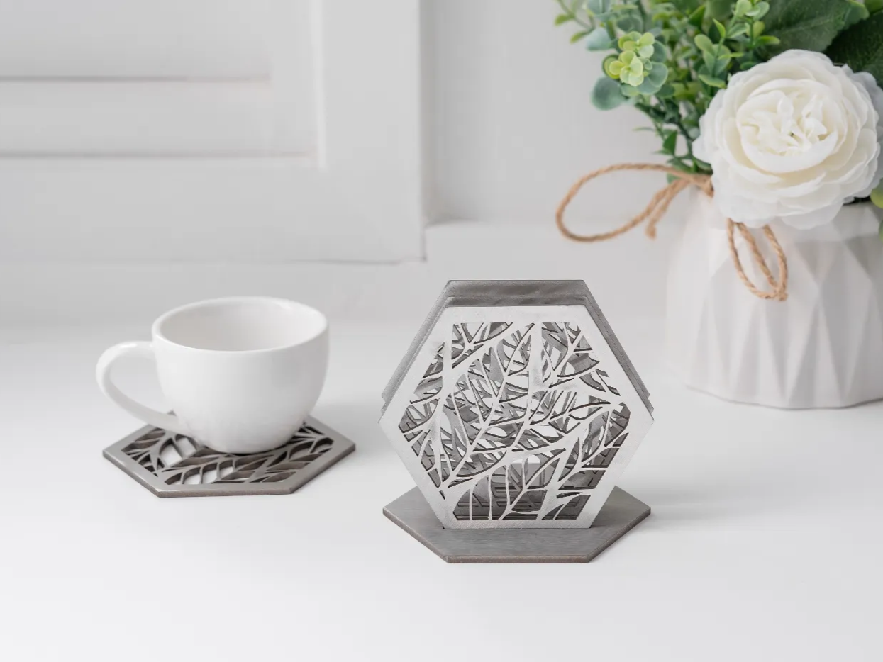 Set of hexagonal metal coasters with a leaf cutout pattern and matching holder