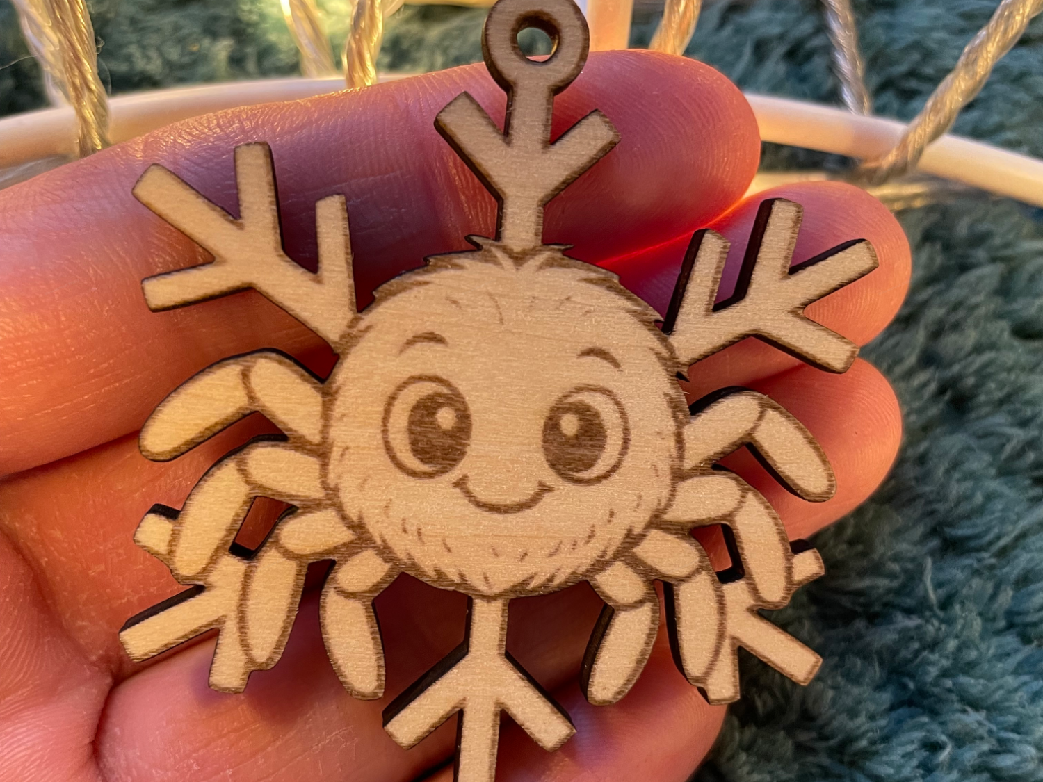 A small wooden snowflake ornament engraved with a cute smiling face, held in a hand