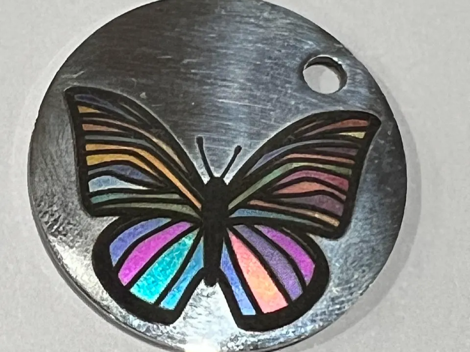 A stainless steel medallion with a rainbow-colored engraved butterfly