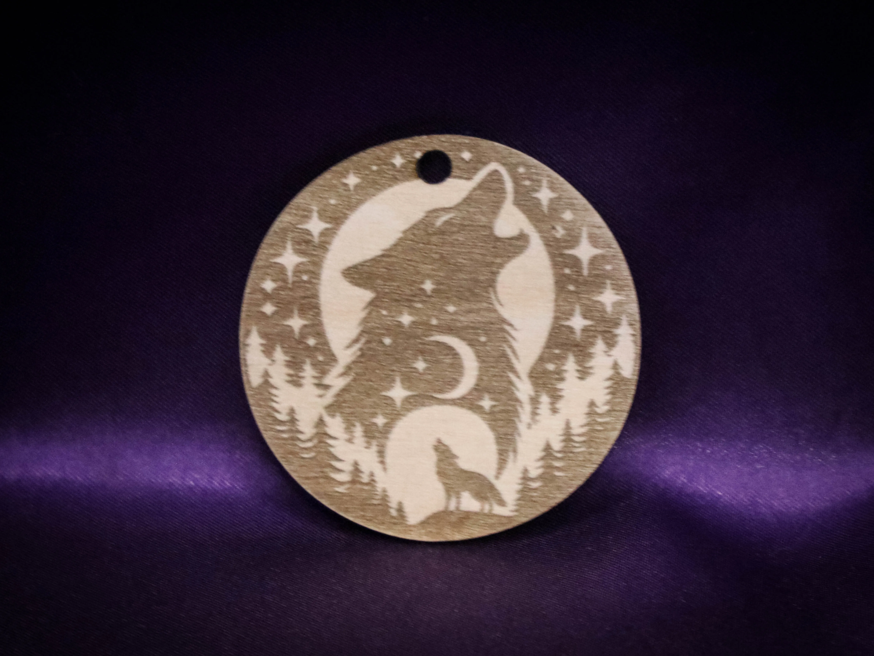 Round wood ornament engraved with a howling wolf and forest moon