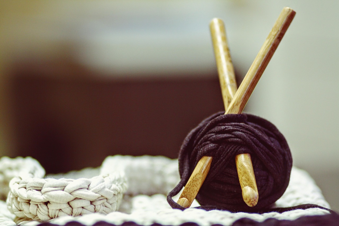 A ball of yarn with two crochet hooks resting on a crocheted piece