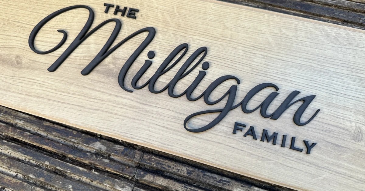 A wooden family name sign combining a large script name with small sans-serif capitals