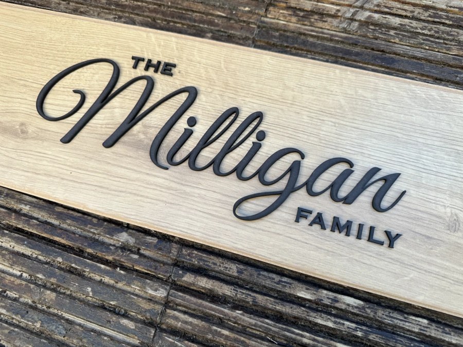 A finished wooden family name sign combining a script name with sans-serif capitals