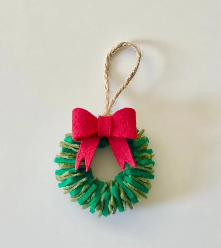 A handmade felt wreath ornament with a red bow and twine hanging loop