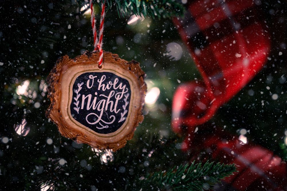 A wooden Christmas ornament hanging on a fir branch in gentle snowfall
